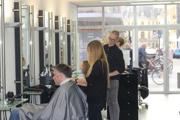 Friseursalon mit mehreren Kunden beim Haareschneiden in moderner, heller Umgebung.